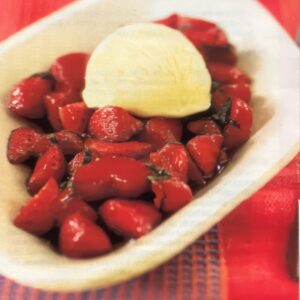 Ravier blanc contenant une boule de glace vanille déposée par dessus des fraises au vinaigre balsamique