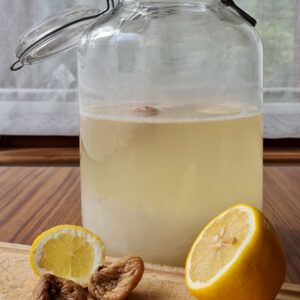 Bocal contenant du kéfir de fruit avec citron et figues flottant dans le liquide. A l'avant-plan, un citron coupé en 2 et 2 figues sèches