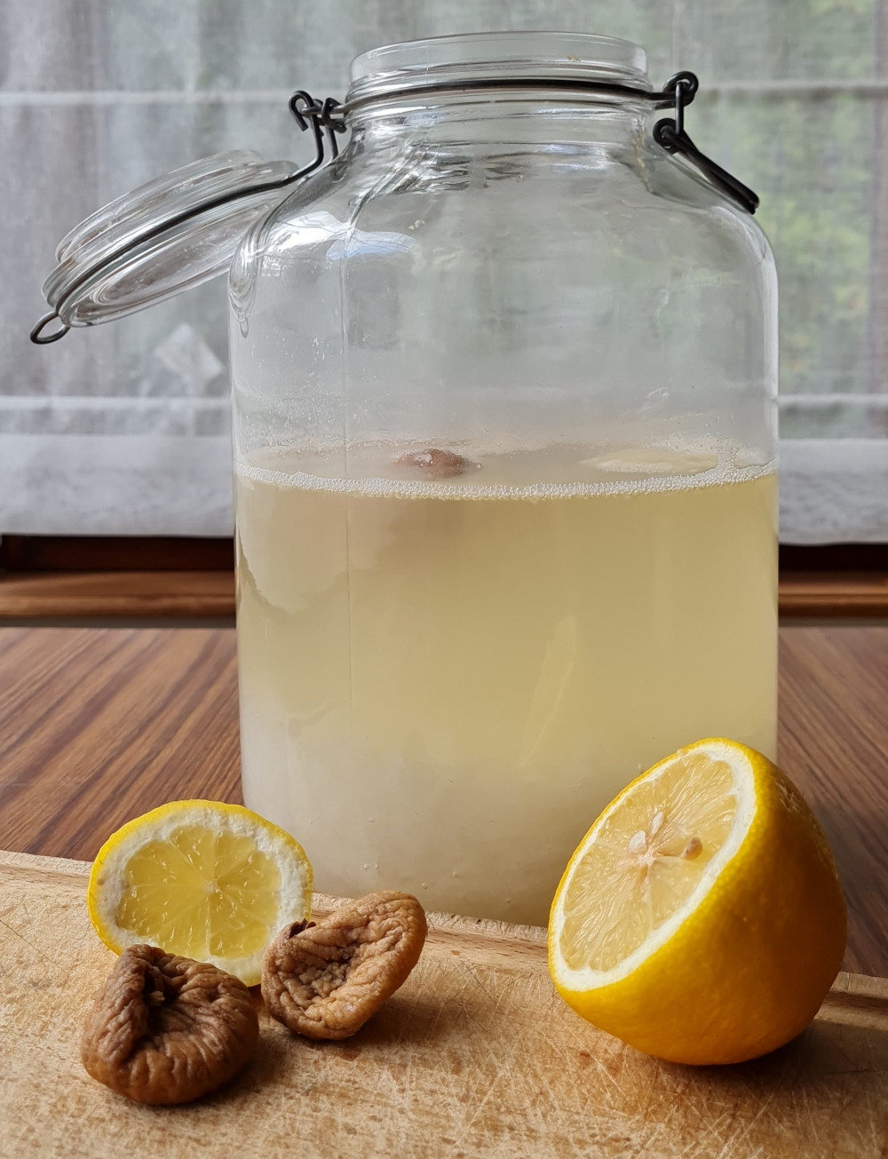Bocal contenant du kéfir de fruit avec citron et figues flottant dans le liquide. A l'avant-plan, un citron coupé en 2 et 2 figues sèches