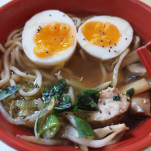 Bol contenant des ramens avec des petits légumes, morceaux de dinde et un oeuf dur coupé en deux